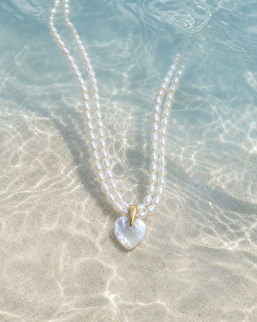 Heart pearl necklace resting on sand under clear sunlit water